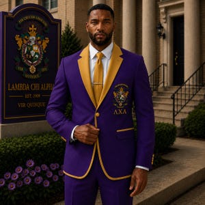 Puede incluir: Una chaqueta de traje morada con solapas doradas, una camisa blanca y una corbata dorada con pasador. La chaqueta presenta un escudo bordado en dorado en el pecho izquierdo y las letras griegas AXA en hilo dorado, con botones dorados.