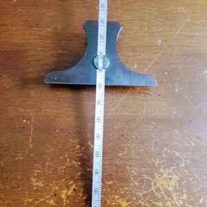 May include: A metal marking gauge with a ruler marked in inches. The gauge is dark gray and has a wide base with a central screw. The ruler extends to 5.5 inches.
