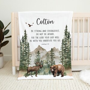 May include: A white baby blanket with a watercolor forest scene, a moose, a bear, and the text "Cotton" and "BE STRONG AND COURAGEOUS. DO NOT BE AFRAID, FOR THE LORD YOUR GOD WILL BE WITH YOU WHEREVER YOU GO. Joshua 1:9".