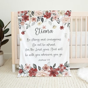May include: A white baby blanket with a floral design in shades of pink, red, and gray. The blanket features the name "Eliana" and the Bible verse "Be strong and courageous. Do not be afraid, for the Lord your God will be with you wherever you go. Joshua 1:9."