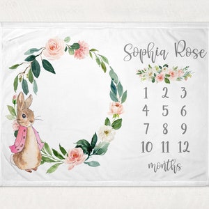 May include: A white baby milestone blanket with a floral wreath, a bunny rabbit, and the text "Sophia Rose" and "12 months".