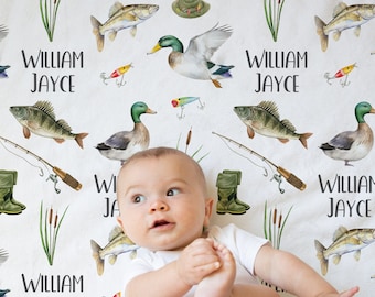 May include: A white baby blanket with a fishing theme. The blanket features a repeating pattern of fish, ducks, fishing rods, and boots. The name "William Jayce" is repeated throughout the blanket.