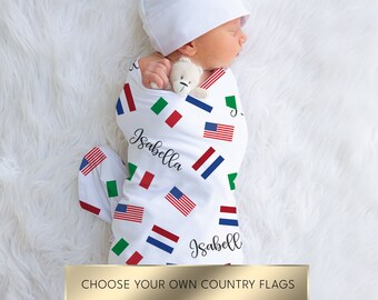 May include: A white swaddle blanket with a pattern of various country flags, including the American flag, the Italian flag, and the Dutch flag. The blanket is wrapped around a sleeping baby with the name "Isabella" written on the blanket.