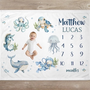 May include: White baby milestone blanket featuring watercolor illustrations of sea creatures like an octopus, turtle, seahorse, whale, and diver. The blanket includes the name "Matthew Lucas" and numbers 1-12 for monthly photos.