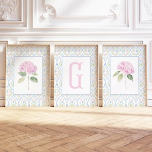 May include: A set of three rectangular wall art prints featuring a light blue and pink floral trellis pattern border. The two outer prints display a single pink hydrangea flower with green leaves, while the center print features a large pink letter G.