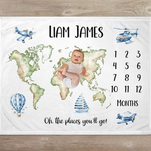 May include: A white baby blanket with a world map design, blue airplanes, a hot air balloon, a sailboat, and a helicopter. The blanket also has the text "Liam James" and "Oh, the places you'll go!" and a number chart for tracking a baby's monthly growth.