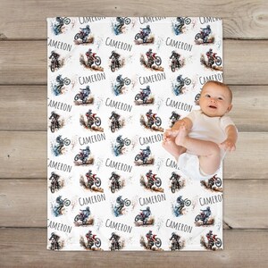 May include: White baby blanket with a repeating pattern of watercolor illustrations of dirt bikes and the name "Cameron".