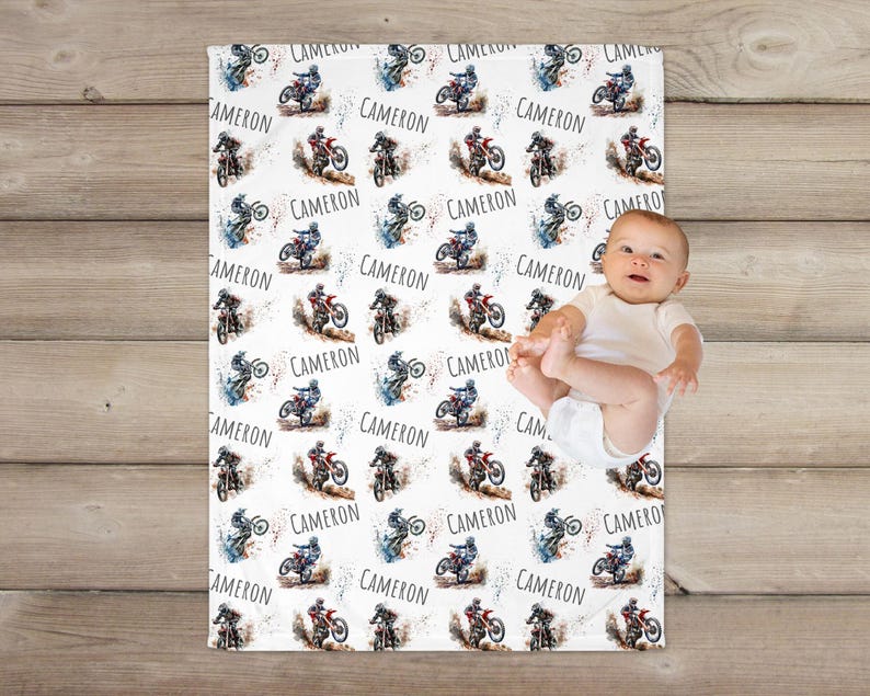 May include: White baby blanket with a repeating pattern of watercolor illustrations of dirt bikes and the name "Cameron".