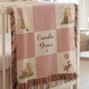May include: Pink and beige woven baby blanket with Winnie the Pooh characters. The blanket features a patchwork design with the name "Camila Grace" and a heart. Winnie the Pooh and Tigger are shown with balloons and honey.
