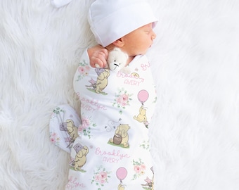 May include: A newborn baby wrapped in a white swaddle blanket and matching hat. The blanket features a Winnie the Pooh design with pink flowers and the names "Brooklyn" and "Avery". The baby is also holding a small stuffed animal.