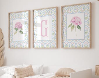 May include: A set of three framed wall art prints featuring a light blue and pink floral damask pattern border. The left and right prints display a single pink hydrangea, while the center print features a large, light pink letter G.