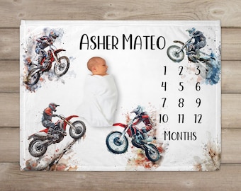 May include: White baby blanket with a watercolor design featuring motocross bikes and the name "Asher Mateo". The blanket also includes numbers 1-12 for tracking a baby's growth.
