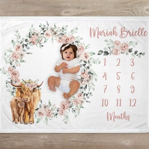 May include: White baby milestone blanket with a floral wreath design. The blanket features a watercolor illustration of a Highland cow and calf, along with the name "Mariah Brielle" and numbers 1-12 for monthly photos.