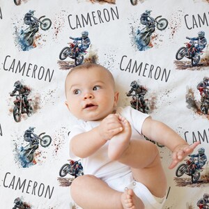 May include: A white baby blanket with a watercolor design of dirt bikes and the name "CAMERON" repeated throughout.