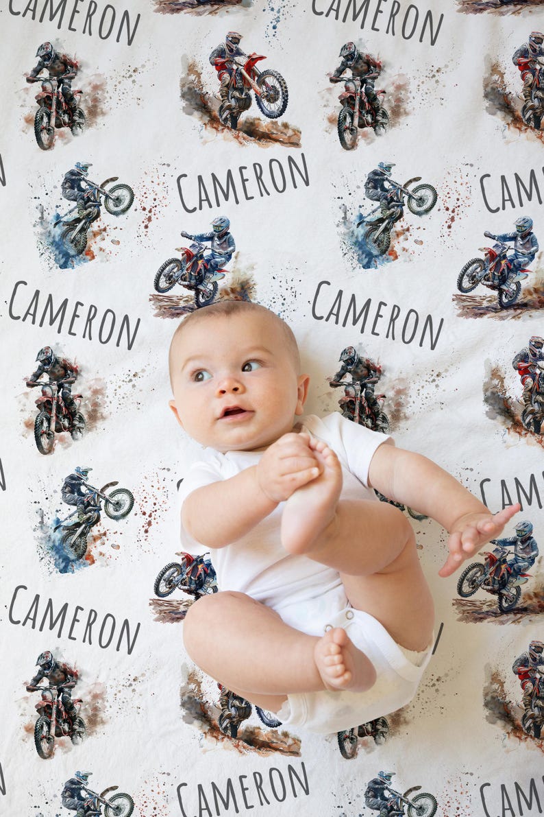 May include: A white baby blanket with a watercolor design of dirt bikes and the name "CAMERON" repeated throughout.