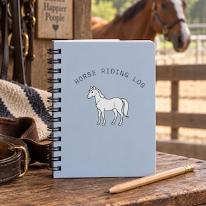 May include: A light blue spiral-bound notebook with the text HORSE RIDING LOG and a line drawing of a horse on the cover. A wooden pencil with a pink eraser lies on the surface next to the notebook, which features a black metal coil binding.