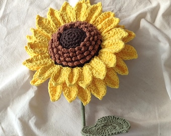 May include: A handcrafted crochet sunflower with yellow petals, a brown center, and a green stem and leaf. The sunflower is made of yarn and is a decorative item.