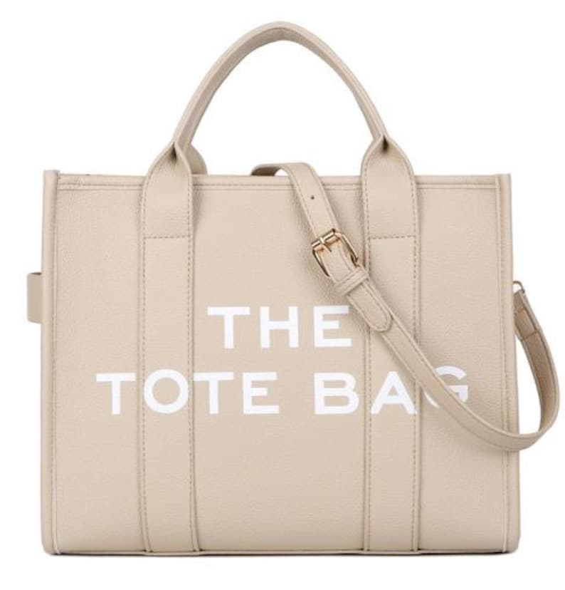 Pu&ograve; includere: Borsa tote beige con la scritta bianca "THE TOTE BAG". La borsa ha due manici superiori e una tracolla staccabile con fibbia color oro. La borsa &egrave; realizzata in un materiale strutturato.