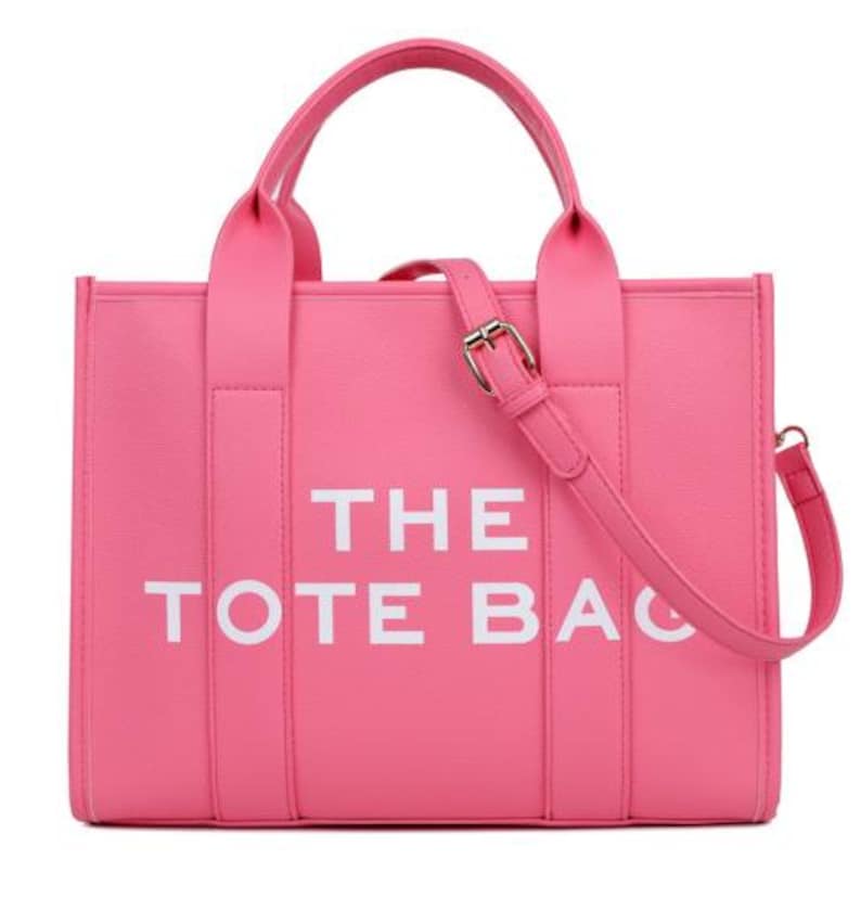 Pu&ograve; includere: Una borsa tote rosa acceso con la scritta bianca "THE TOTE BAG". La borsa ha due manici superiori e una tracolla staccabile con fibbia dorata. La borsa &egrave; realizzata in materiale liscio.
