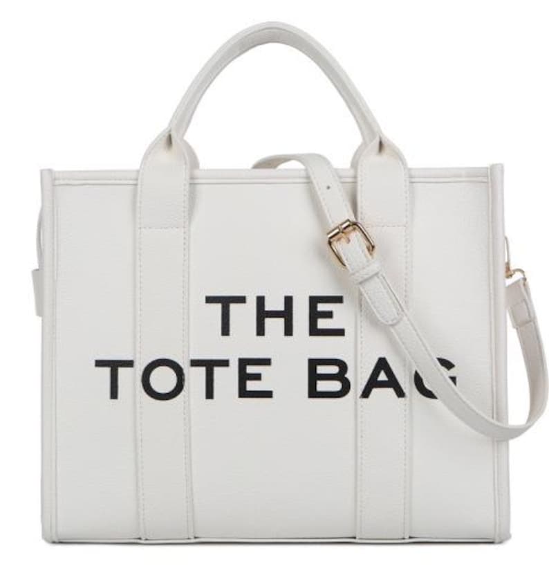 Pu&ograve; includere: Borsa tote bianca con la scritta "THE TOTE BAG" in nero. La borsa ha un manico superiore e una tracolla staccabile con fibbia color oro. La borsa &egrave; rettangolare e ha un design semplice e pulito.
