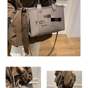 May include: Gray tote bag with top handles and a shoulder strap. The bag features the text "TOT MARC J" on the front. The bag is held by a person wearing a brown coat and white pants.