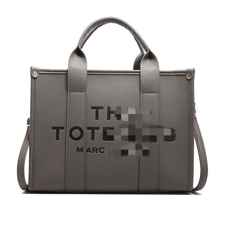 May include: Gray tote bag with top handles and a detachable shoulder strap. The bag features the words "THE TOTE MARC" in a bold, cut-out font. The bag has a rectangular shape and is made of a textured material.