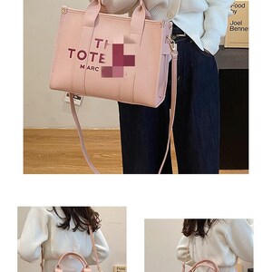 May include: A light pink tote bag with the words "TI TOTE MARC" printed on the front. The bag has a top handle and a detachable shoulder strap. The bag is made of a smooth material and has a rectangular shape.