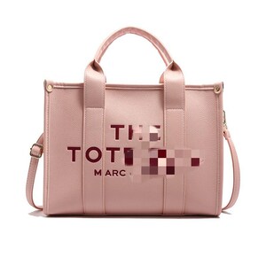 May include: A light pink tote bag with the words "THE TOTE" and "MARC" printed on the front. The bag has two handles and a detachable shoulder strap. The hardware is gold-colored.