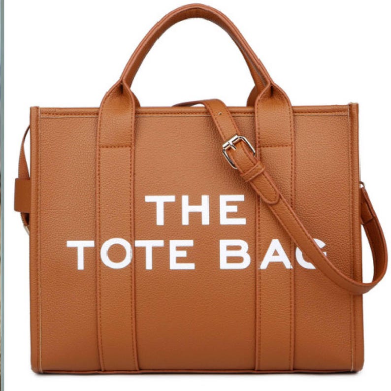 Pu&ograve; includere: Borsa tote marrone con le parole bianche "THE TOTE BAG". La borsa ha un manico superiore e una tracolla staccabile. La borsa &egrave; realizzata in un materiale strutturato e ha una fibbia argentata.