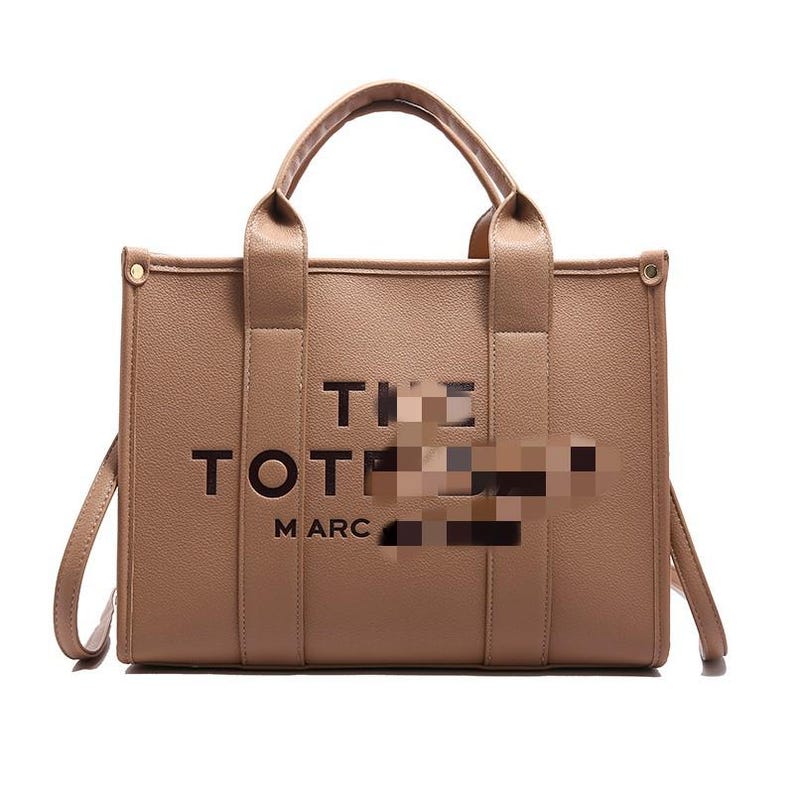 May include: A tan tote bag with the words "THE TOTE MARC" printed on the front. The bag has two top handles and a detachable shoulder strap. The bag is made of a smooth material and has a rectangular shape.