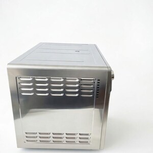 May include: A stainless steel countertop oven with a rectangular shape. The front panel features horizontal vent slots. The oven is designed with a sleek, modern aesthetic, suitable for kitchen appliances.