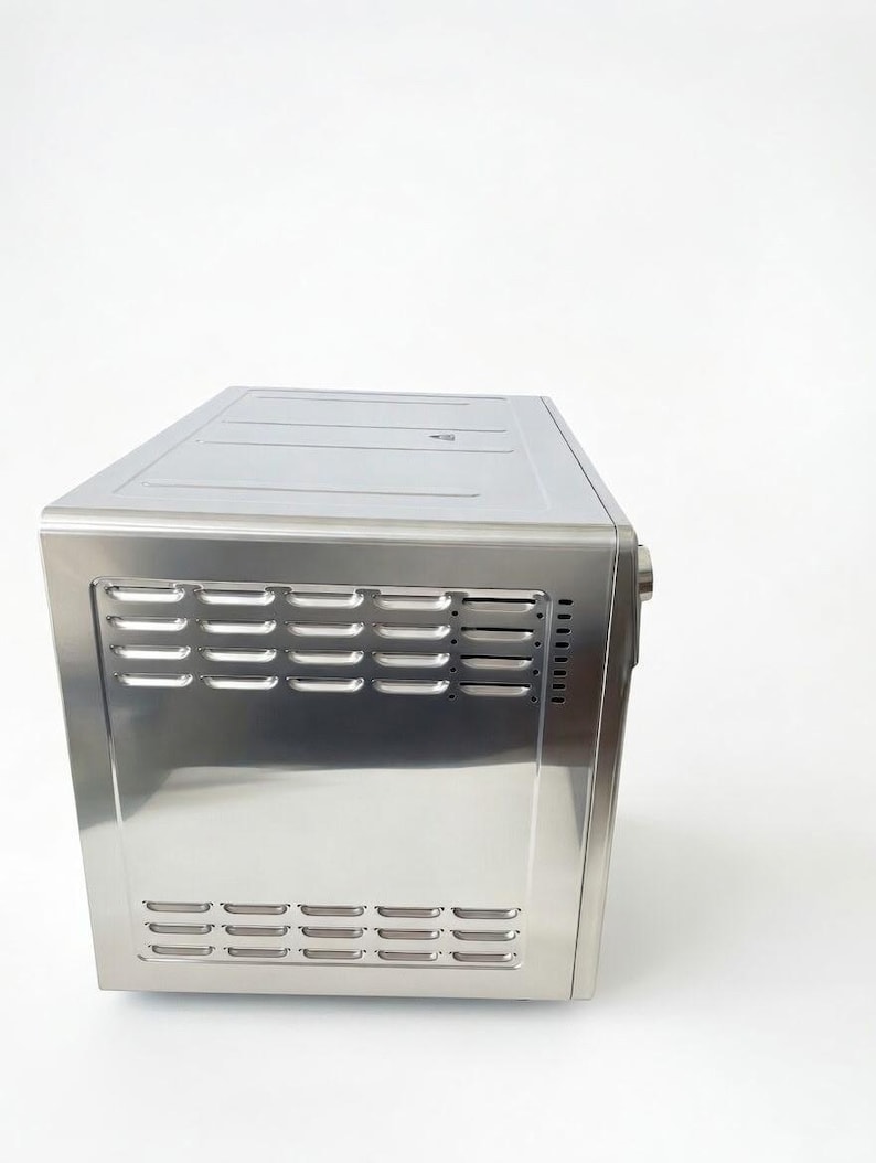 May include: A stainless steel countertop oven with a rectangular shape. The front panel features horizontal vent slots. The oven is designed with a sleek, modern aesthetic, suitable for kitchen appliances.
