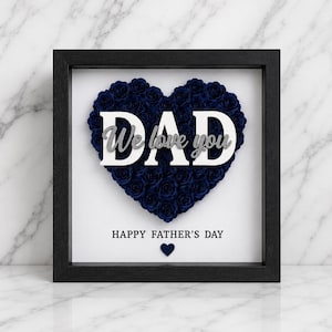 May include: A framed Father's Day gift featuring a heart-shaped arrangement of dark blue roses. The word "DAD" is prominently displayed, with "We love you" above it. The phrase "HAPPY FATHER'S DAY" is below, with a small heart.