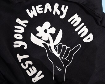 May include: Black hoodie with a white graphic of a hand holding a flower with the text "Rest your weary mind" around it.