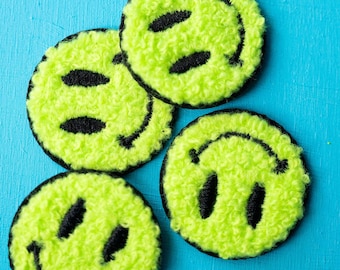 May include: Four green fuzzy smiley face patches with black outlines on a blue background.