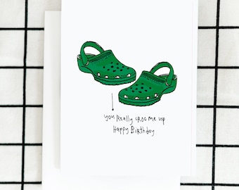 May include: A green and white birthday card with a drawing of two green Crocs and the text "you really croc me up Happy Birthday".