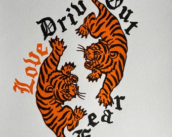 May include: Two orange and black tigers facing each other with the text "Love Drives Out Fear" in black gothic lettering.