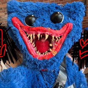 May include: A large, plush blue monster head with black eyes and a wide, red-lined mouth filled with sharp, white teeth. The monster has a furry texture and a menacing expression, likely a costume or prop.