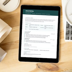 May include: A tablet displaying a resume, with the name "Alexia Sterling" at the top. The tablet is on a wooden surface, next to rolled paper, a small white dish, and a pen.