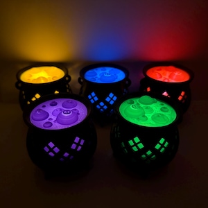 May include: Five black cauldron-shaped containers with cut-out diamond patterns on the sides. Each cauldron emits a different colored light from within, including yellow, blue, red, purple, and green, illuminating the bubbling liquid surface.