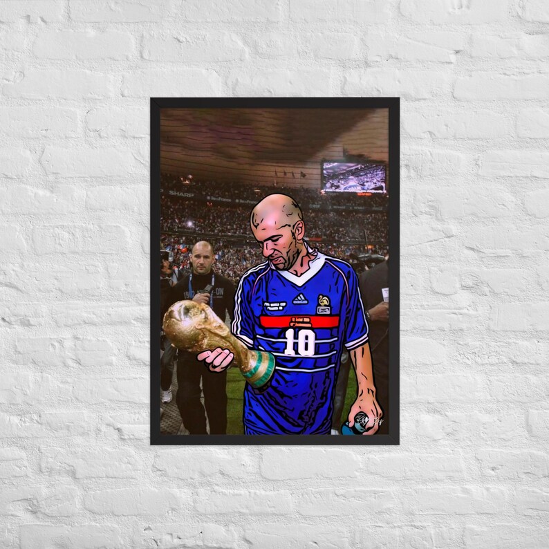 Op de afbeelding: Een ingelijste poster met een gestileerde illustratie van een voetballer in een blauw shirt met het nummer 10, die een gouden trofee vasthoudt. De speler heeft een kaal hoofd en staat in een stadion met publiek op de achtergrond.