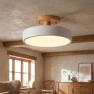 May include: A contemporary ceiling light. It features a white, circular shade and a wooden base. The light is mounted on a light-coloured ceiling, providing soft ambient lighting. The flush mount design is suitable for various interior styles. The diameter is approximately 40 cm.