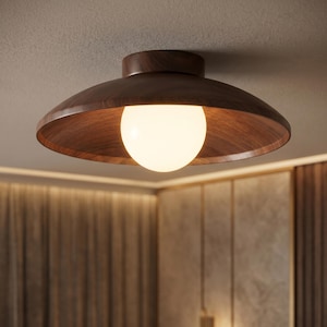 May include: A flush-mount ceiling light fixture with a dark brown wooden shade and a spherical, glowing white light bulb. The shade has a shallow, bowl-like shape. The fixture is mounted on a white ceiling.