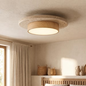 Puede incluir: Una moderna lámpara de techo con diseño circular. Tiene un anillo exterior de color beige claro similar a la piedra, una sección media de madera y una fuente de luz blanca brillante. La lámpara está montada en un techo blanco.
