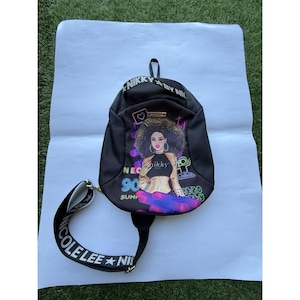 May include: Black backpack with a graphic of a woman with curly hair, wearing a crop top. The backpack has a top handle and a shoulder strap with the text "COLE LEE NII". The backpack also has the text "NIKKY BY NIK" and "NEO 90 SUMM 20 LY".