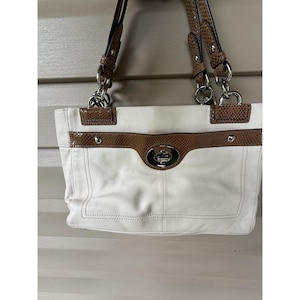 May include: White leather handbag with brown snakeskin-patterned accents and silver-tone hardware. Features a top handle and a front flap with a turn-lock closure. The bag has a structured shape and a spacious interior.