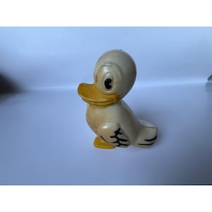 May include: A vintage ceramic duck figurine in a seated position. The duck has a cream-colored body, a yellow beak and feet, and black accents on the eyes and wings. The figurine is a classic collectible.