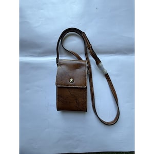 Op de afbeelding: Een bruine leren crossbodytas met een kaartontwerp. De tas heeft een klepsluiting met een goudkleurige knoop en een lange, verstelbare riem. Witte stiksels accentueren de randen van de tas en de riem.
