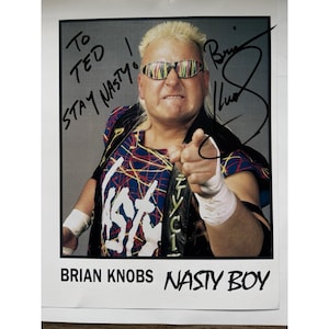 May include: A signed photograph of Brian Knobs, also known as Nasty Boy. The image features Knobs wearing sunglasses and a colorful jacket, pointing at the viewer. The photo includes the text "To Ted, Stay Nasty!" and "Brian Knobs Nasty Boy."