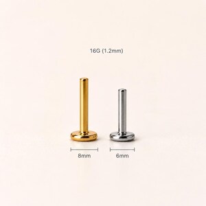 May include: Two labret studs, one gold-colored and one silver-colored, are displayed. The gold stud has a base of 8mm, while the silver stud has a base of 6mm. The text "16G (1.2mm)" is above the studs, indicating the gauge and thickness.